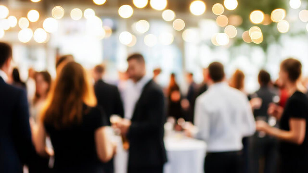 Blurry photo of cocktail party guests beneath warm string lights
