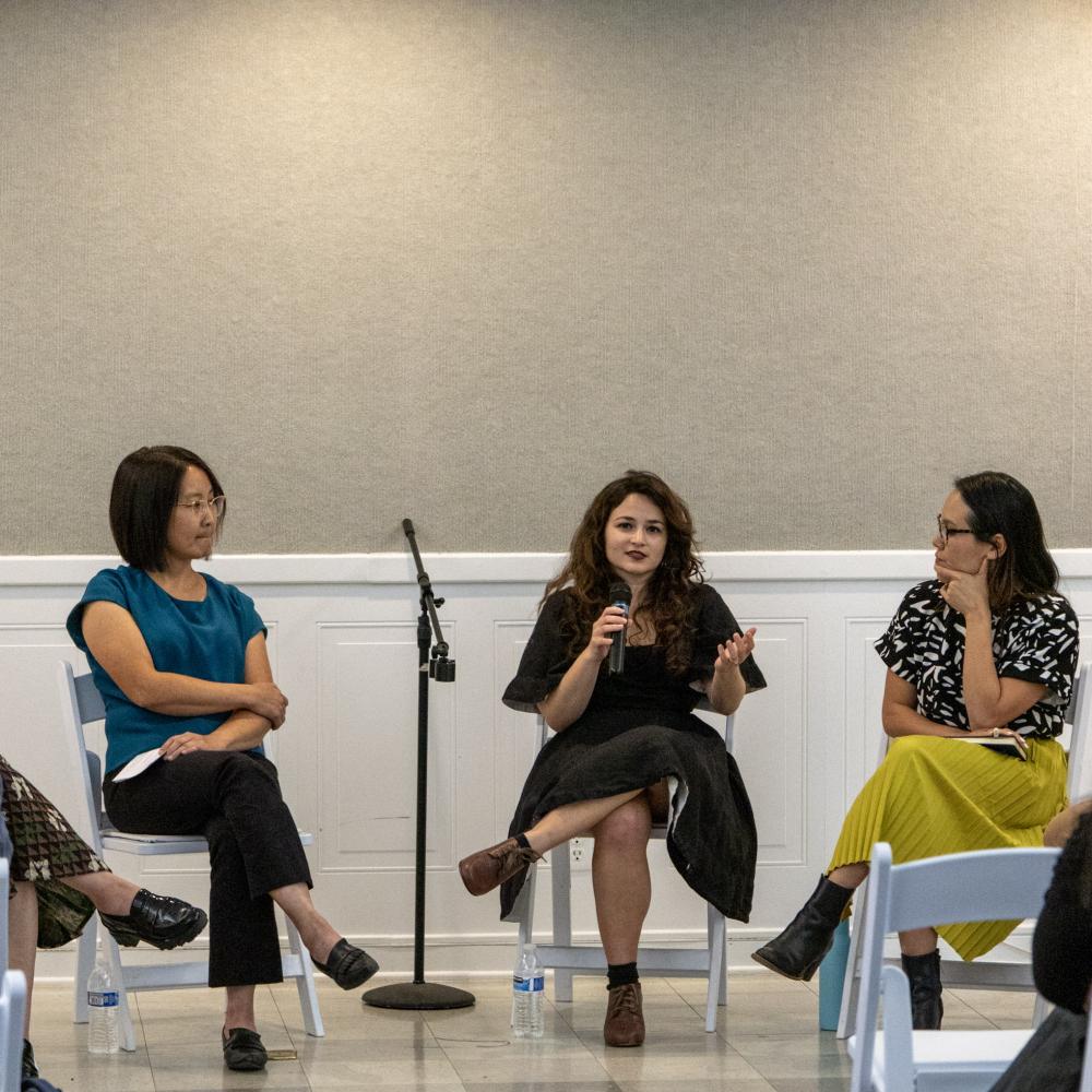 Three women seated in panel discussion; center woman speaks into microphone