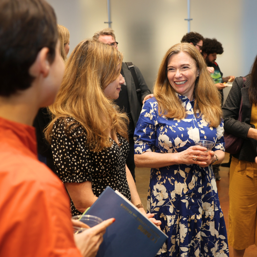 Smiling woman in blue floral dress chatting with colleagues at an indoor gathering