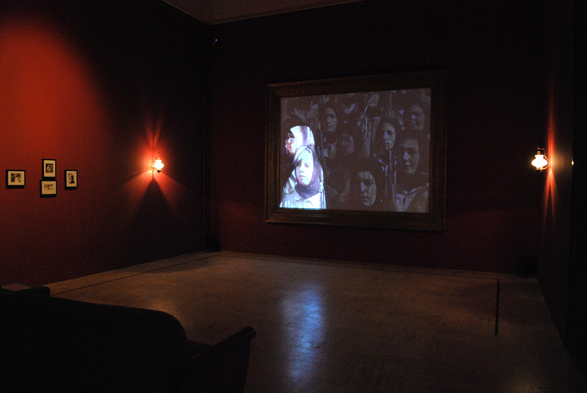 In a dark room, an image of many women wearing headscarves is projected, with one woman's face being highlighted