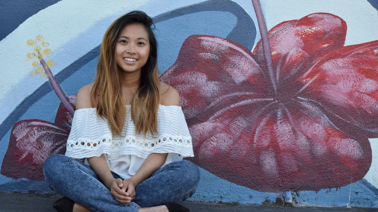 Katherine Nasol sits in front of a mural of hibiscus flowers