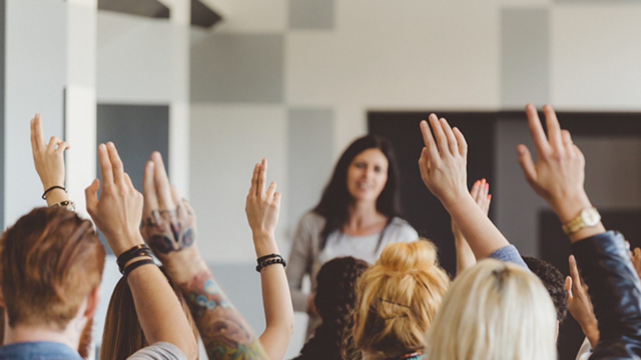 Person standing in front of seated students with hands raised