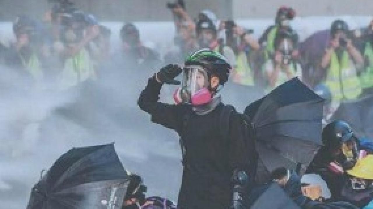 Protesters with umbrellas wearing helmets and gas masks