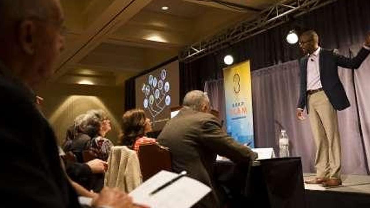 Speaker on a stage presents to room of listeners