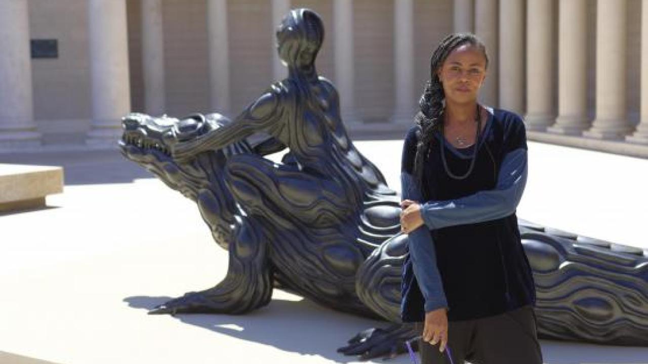 Photo of Wangechi Mutu, in front of a sculpture of someone riding an alligator