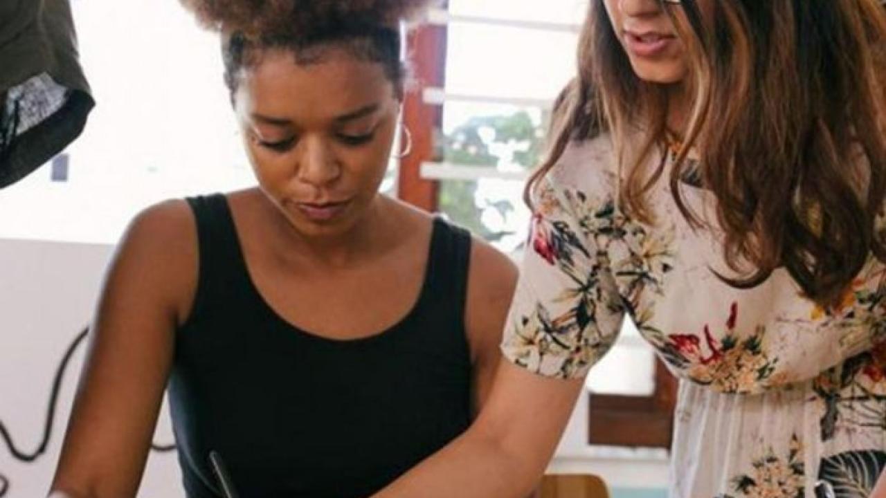 A young Black woman receives feedback on writing from a young White woman