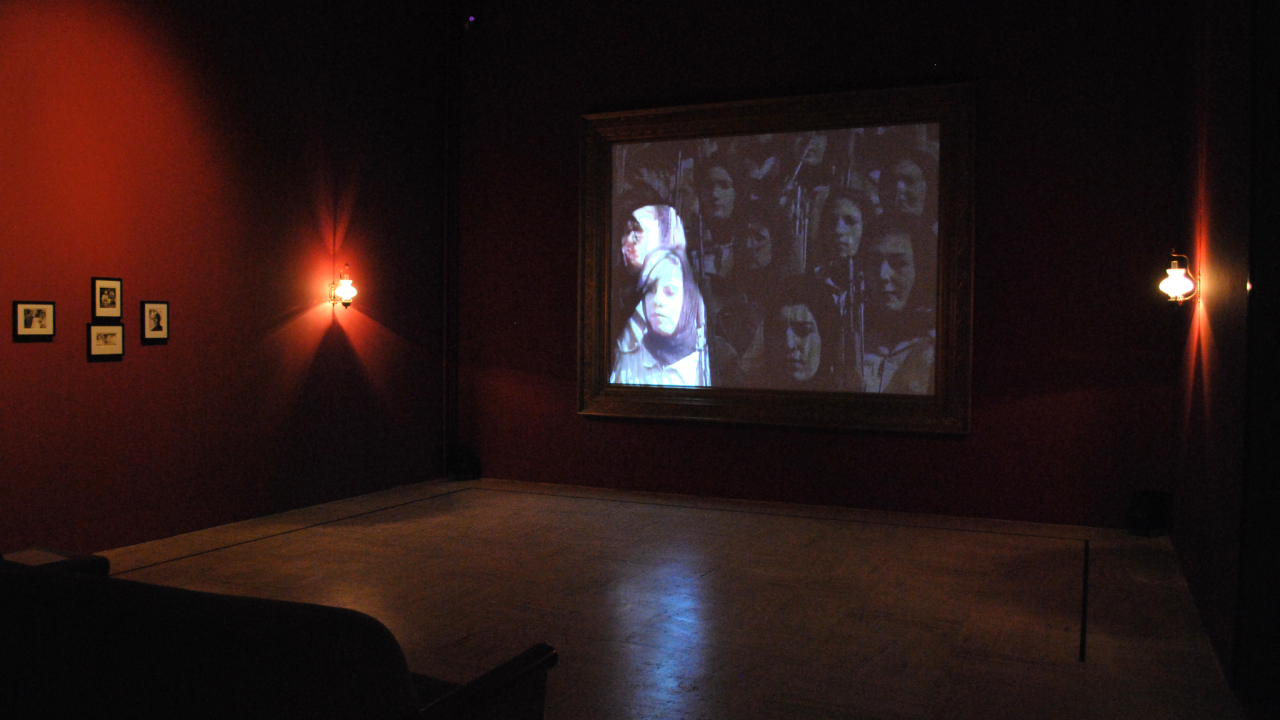 In a dark room, a woman's image is projected onto a screen