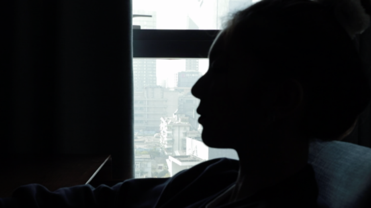 A black and white photo of a silhouetted person looking out a window