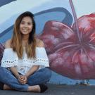 Katherine Nasol sits in front of a mural of hibiscus flowers